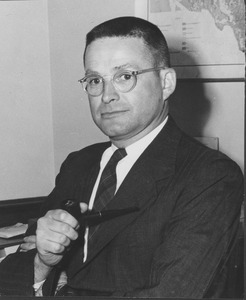 Hugh Montgomery seated holding a pipe