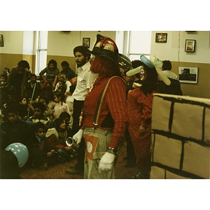 Audience, consisting mostly of Hispanic American children and some adults, watches two clowns and a group of adults at the Three Kings' Day celebration at La Alianza Hispana, Roxbury, Mass.