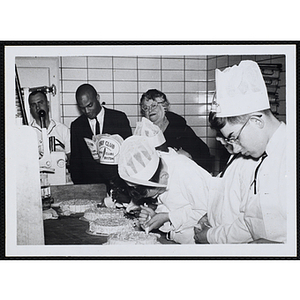 Members of the Tom Pappas Chefs' Club decorate cakes in a Brandeis University kitchen as Chefs' Club committee member Mary A. Sciacca looks on with two unidentified men