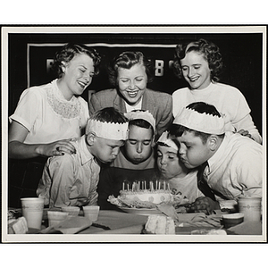 Four boys blow candles on a cake as three women look on