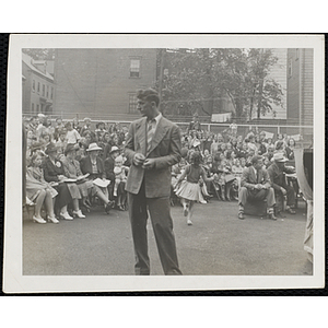 A man, facing away from the audience, looks off to his right at a Boys' Club Little Sister Contest