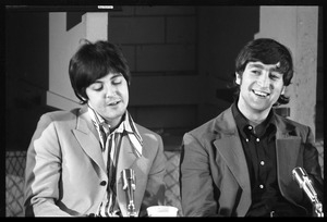 Paul McCartney (left) and John Lennon seated at a table, during a Beatles press conference
