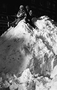 Unidentified children sitting on large snow pile