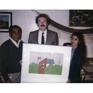 Clara Garcia and two unidentified men hold up a limited edition serigraph designed by Joaquin Reyes which depicts Villa Victoria.