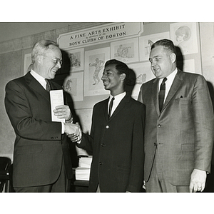 Dwight C. Shepler, at far left, shakes hands with Tyrone Simmons while Robert A. Price looks on at the Boys' Clubs of Boston Fine Arts Exhibit at the State Street Bank and Trust Company