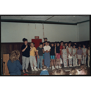 A woman speaks into a microphone while standing with participants in the Charlestown Boys and Girls Club Talent Show