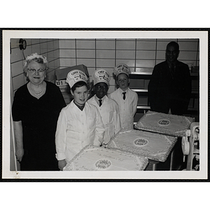 Three members of the Tom Pappas Chefs' Club, Chefs' Club Committee member Mary A. Sciacca and an unidentified man pose with three decorated cakes in a kitchen