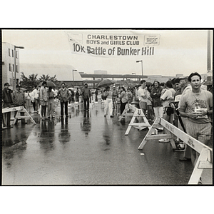 Spectators and runners gather beneath a "10K Battle of Bunker Hill" road race banner