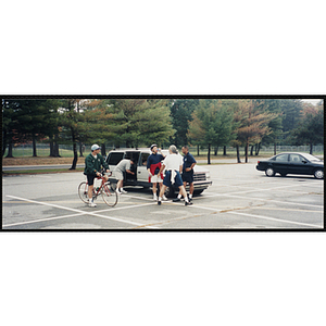 Three men stand next to a mini van as another man straddles a bike in a parking lot for the Charlestown Bike Race