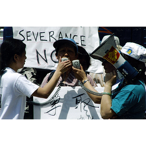 Two women hold megaphones as a Chinese man speaks at a rally protesting for worker' rights at AEI Electronics