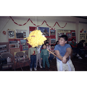 Boy swings a stick at a piñata while other children watch at the Chinese Progressive Association Chinese New Year celebration