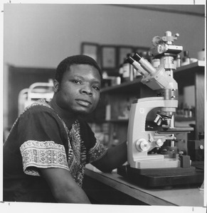 Vincent Saka seated at microscope in lab