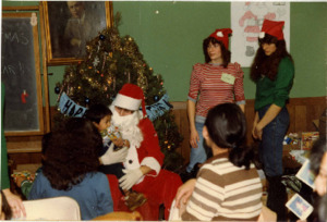 Photograph of a child holding presents and sitting on Santa Claus' lap, [1982-1983].