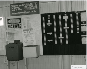 Photograph of a time clock and time card rack, [1982-1983].