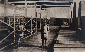 Two soldiers in a large room with empty cots and bunks