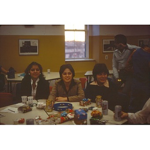 Two young women and a young man seated at a table with gifts at a Christmas party at La Alianza Hispana, Roxbury, Mass.