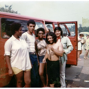 Three male and two female Latino youths stand pose in front of La Alianza's red van in the parking lot adjacent to a park, while on a summer day trip sponsored by La Alianza Hispana.