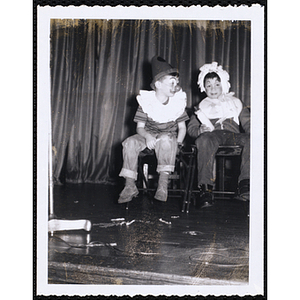 A boy wearing a clown costume looks off to his left while another boy in a baby costume looks at the camera at a Boys' Club's costume contest