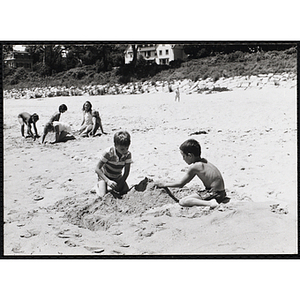 Two boys play with sand on a beach