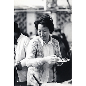 Woman prepares a plate of food for herself at a Chinese Progressive Association event