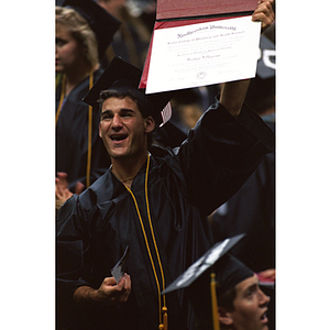 Michael DiPalermo, Class of 1994, surrounded by his fellow graduates holds up his diploma at commencement