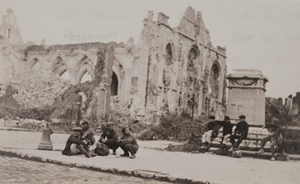 View of boys sitting on the sidewalk in front of an empty monument pedestal and a destroyed stone church in the background