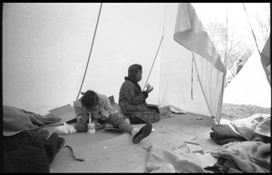 Inside of a strikers' tent, two young women seated on the ground, drinking milk through a straw