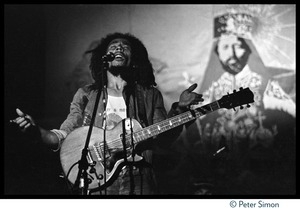 Bob Marley in concert, singing while standing in front of a large banner with a portrait of Haile Selaisse