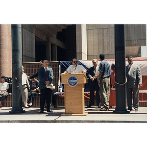 A man speaks from a lectern at City Hall Plaza