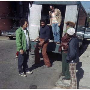 Four men and a boy stand at the rear of a truck containing items to be hauled to a Latino street festival