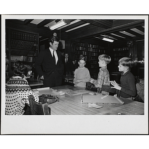 Senator Ted Kennedy talks to three Boys' Club members playing "Wide World Travel Game" while an unidentified woman, seated, looks on