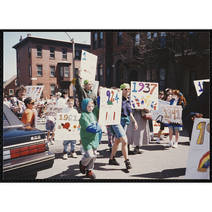 Children and adults holding up their signs while marching down the street during the Boys and Girls Clubs of Boston 100th Anniversary Celebration Parade