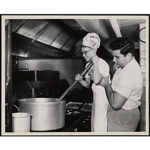 A member of the Tom Pappas Chefs' Club stirs a large pot with the assistance of Brandeis University kitchen staff person