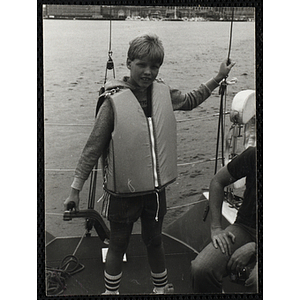 A boy stands on the deck of sailboat in Boston Harbor