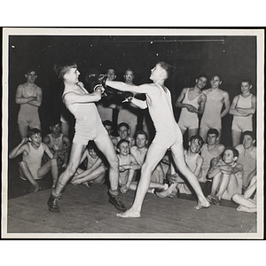 A group of boys in a gymnasium watch two boys throw boxing punches