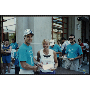 A man shakes a woman's hand as she holds a certificate at the Battle of Bunker Hill Road Race