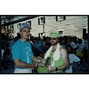 A man holds a trophy as he shakes another man's hand during the Battle of Bunker Hill Road Race