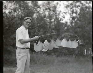 George Allan England holding a stick suspending a series of oversized visors