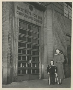 David Grierson, a young boy on crutches, and his mother standing in front of an ICD building