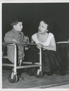 Woman crouched beside young boy in mobility device