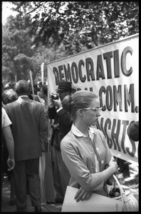 Woman in cats-eye glasses standing in front of a civil rights banner