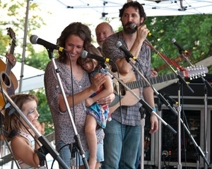 Sarah Lee Guthrie with young girl and Tao Seeger on stage at the Clearwater Festival (Pete Seeger in background)
