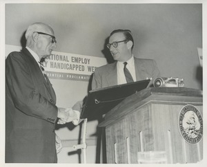 Orin Lehman shaking hands with an unidentified men behind icd podium