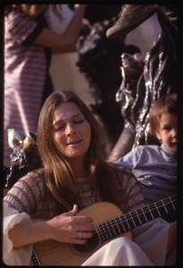 Judy Collins seated at the base of a statue, playing guitar for children