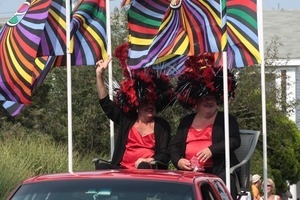 Tim O'Connor and John Michael Gray, the Hat Sisters, in massive feathery wigs and gay pride peace flags, riding in the parade, waving to the crowd : Provincetown Carnival parade
