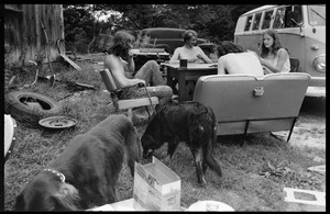 Commune members seated at a card table in front of Montague Farm Commune, dogs in the foreground and Volkswagen microbus behind (Susan Mareneck, far right)
