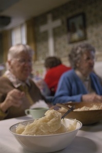 Church supper at the First Congregational Church, Whately: a bowl of mashed potatoes in front of two women seated at a table, eating supper