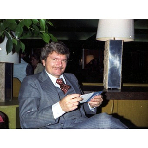 Alianza staff member seated in a chair, smiling, wearing a blue pinstripe suit, and holding a piece of paper
