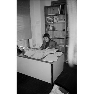Unidentified woman working at her desk among piles of papers.