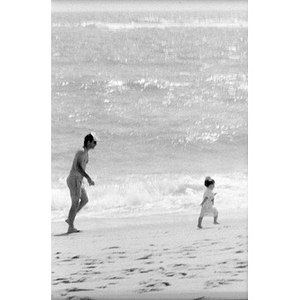 Unidentified man running behind a toddler on the beach.